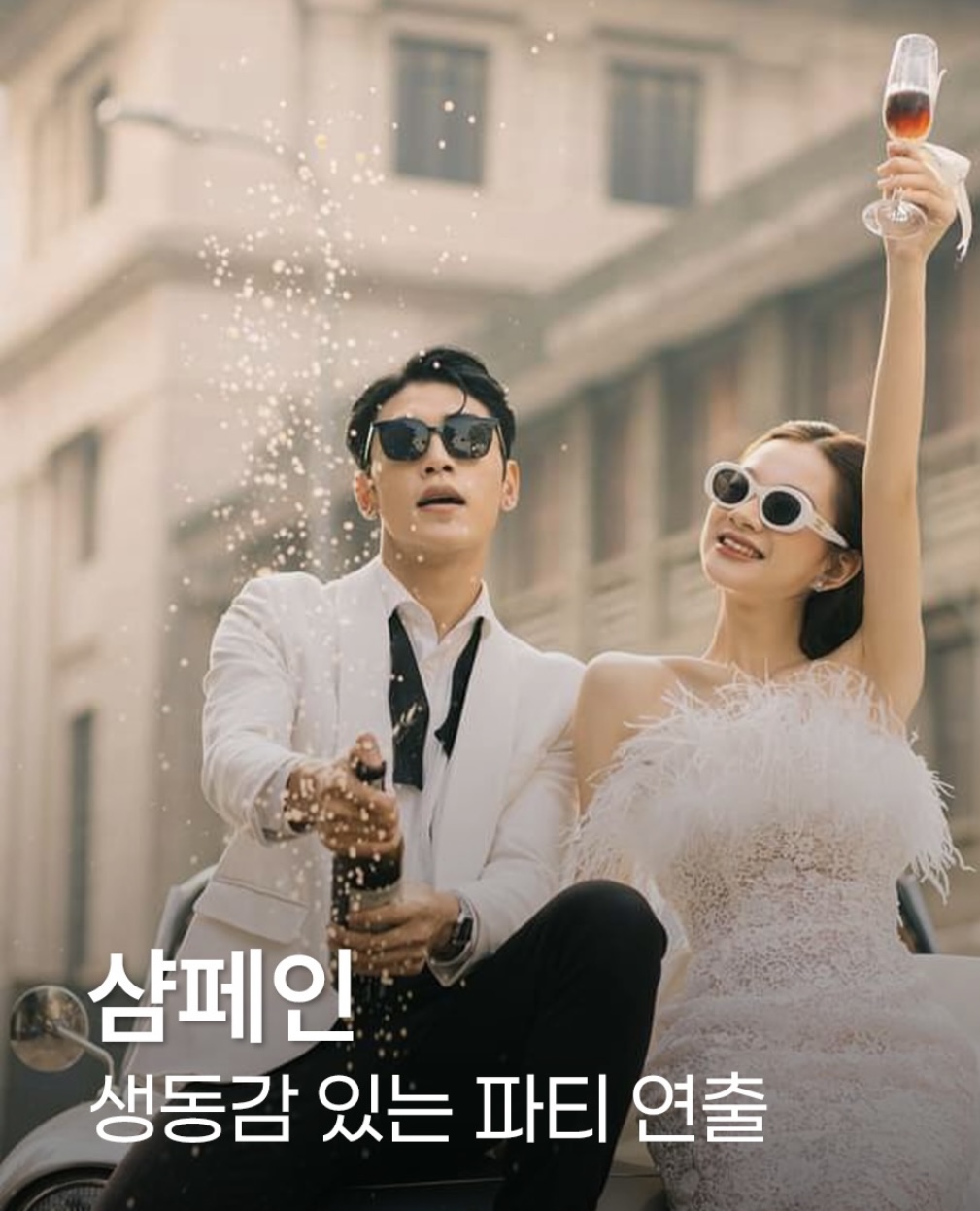 선글라스를 쓴 커플이 나란히 앉아 신랑은 병을 터뜨리고 신부는 잔을 높이 드는 파티 무드 컷이에요. 이미지에 글자가 얹혀 있어요.